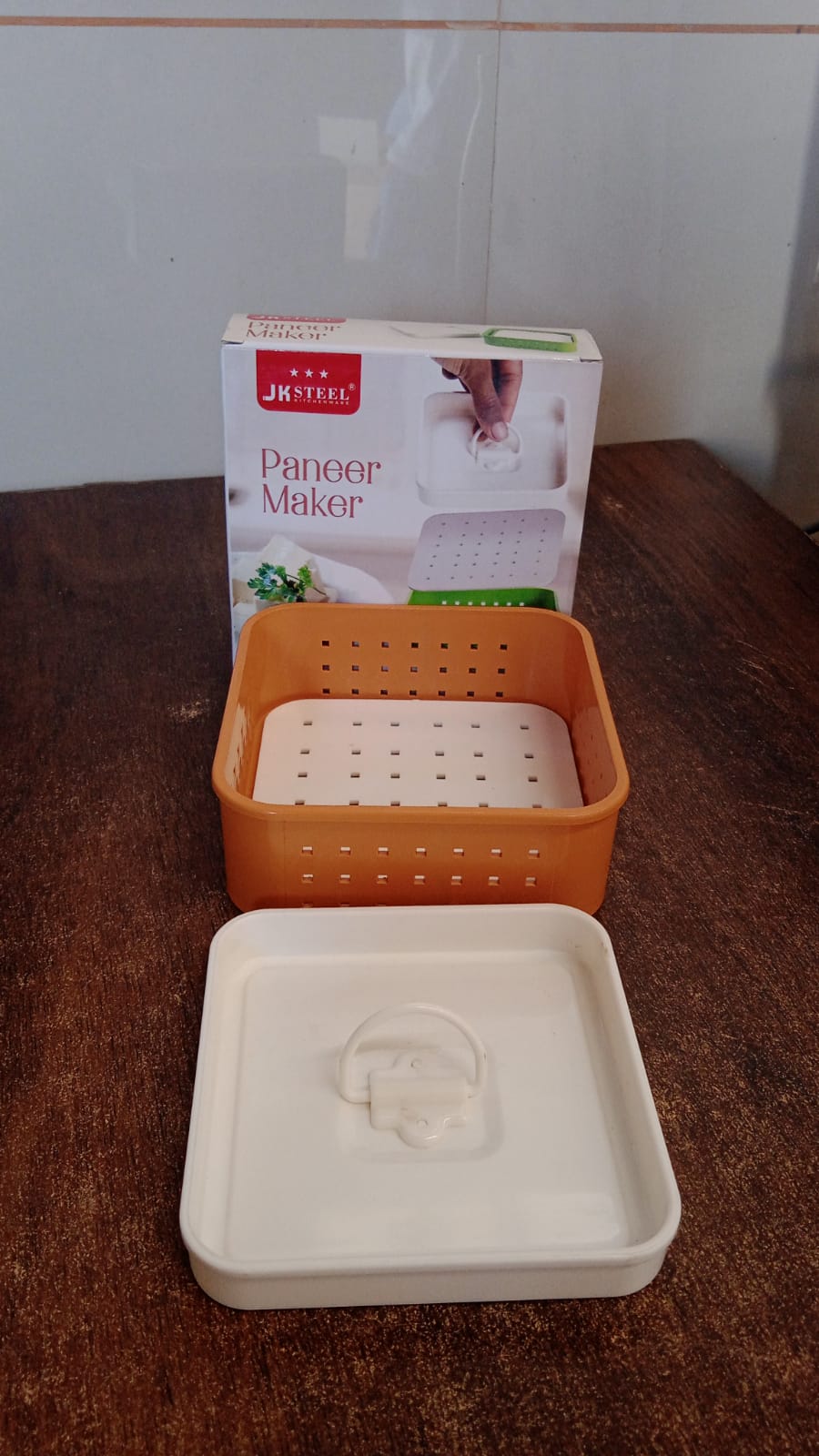 Orange panier maker with white lid on a wooden surface, next to its packaging.