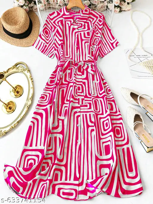 A short-sleeve button-front dress with a matching waist tie, featuring a bold pink and white geometric maze-like pattern. The dress is displayed in a styled flat-lay arrangement alongside a straw hat, gold earrings, a white handbag, and white pointed flats on a white background.
