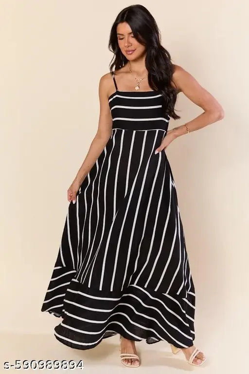 A woman modeling a black and white vertically striped maxi dress with thin spaghetti straps and a flared skirt, posed against a solid beige studio background.